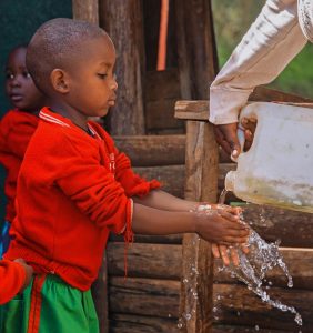 Young child washing hands in a rural area of Uganda, promoting hygiene awareness.